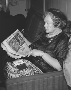 Black and white photo of woman sitting on a sofa reading a newspaper.