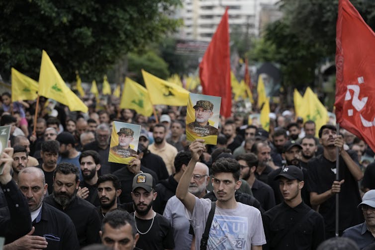 People in a procession carry yellow flags and a picture of a man in military fatigues.