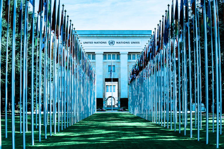 Rows of flags on a green lawn leading up to the United Nations building.