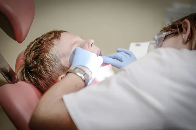A dentist in a white coat inspects a boy's mouth.