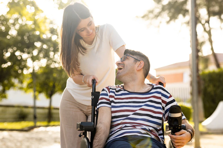 woman smiles at man she is pushing in wheelchair