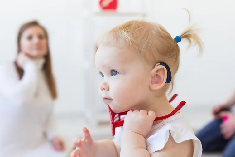woman in back with young child in foreground wearing hearing device
