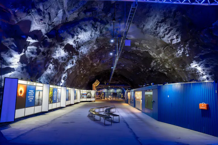 A large underground tunnel lit in blue and white lights with info posters on each side.
