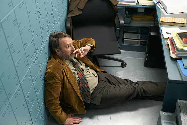 David Mitchell lying on the floor of an office looking stressed
