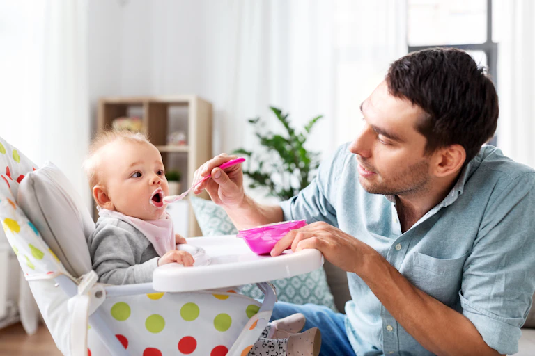 Un papa donne à manger à son enfant installé dans une chaise haute.