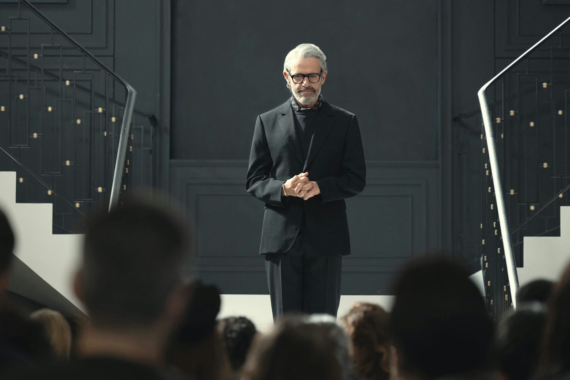 Lambert Wilson stood on the stairs in a black suit.