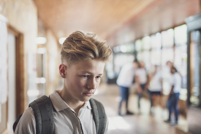 A boy looks bleak while his peers look on in the background.