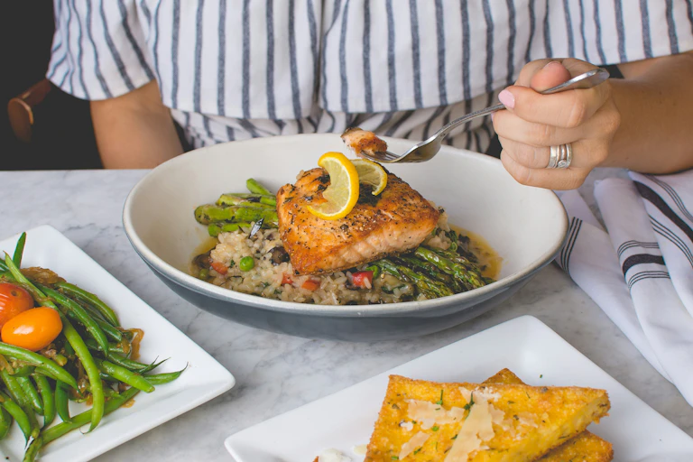 main qui tient une fourchette au dessus d'une assiette de poisson et légumes