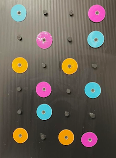 Pink, blue and yellow plastic discs are attached to a black background.