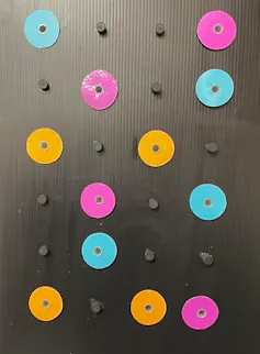 Pink, blue and yellow plastic discs are attached to a black background.