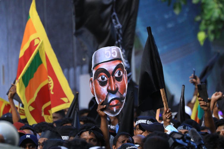 A group of people hold aloft a flag and a giant image of a face.