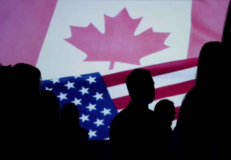 People in silhouette with the Canadian and American flags illuminated beside them.