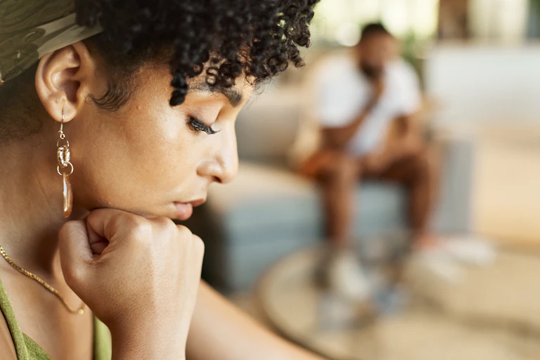 woman looks down with blurred image of man in background