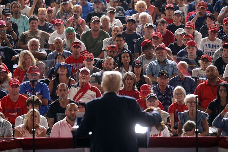 A man wearing a dark suit is seen facing a large crowd of people who all look forward.