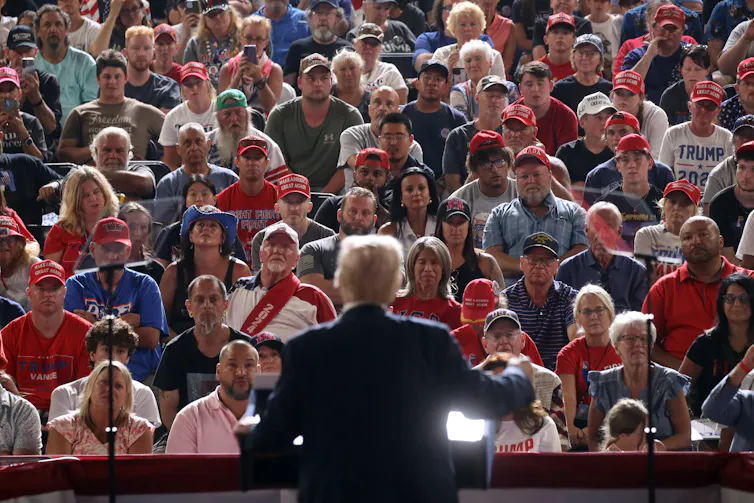 A man wearing a dark suit is seen facing a large crowd of people who all look forward.