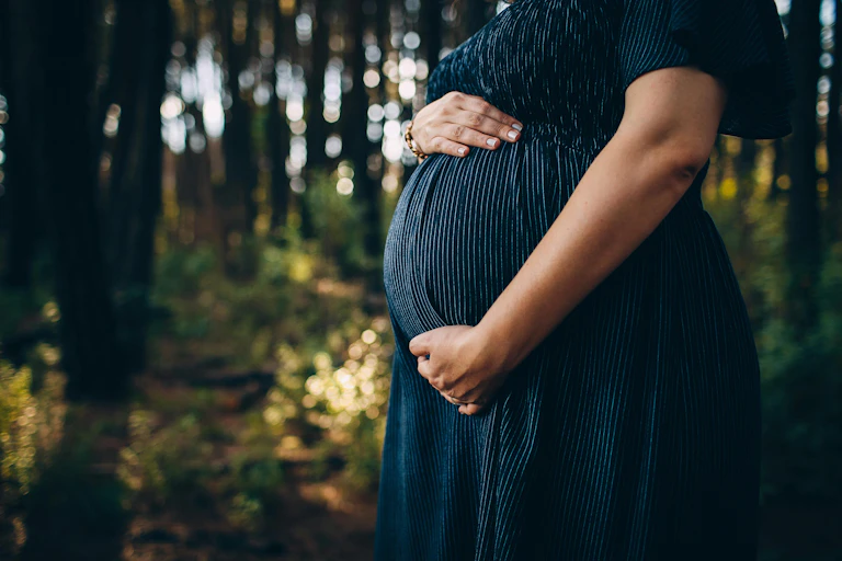 A pregnant woman outdoors holding her stomach.