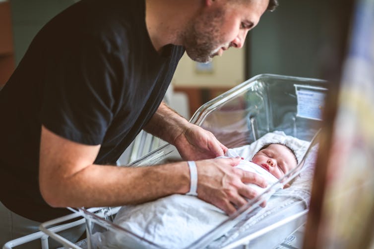 A man is caring for a baby in a hospital crib.