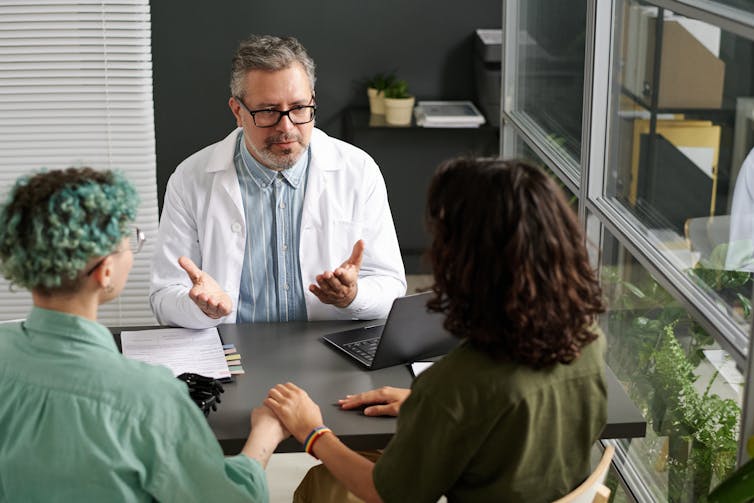 A doctor talks to a non-binary patient and their female partner.