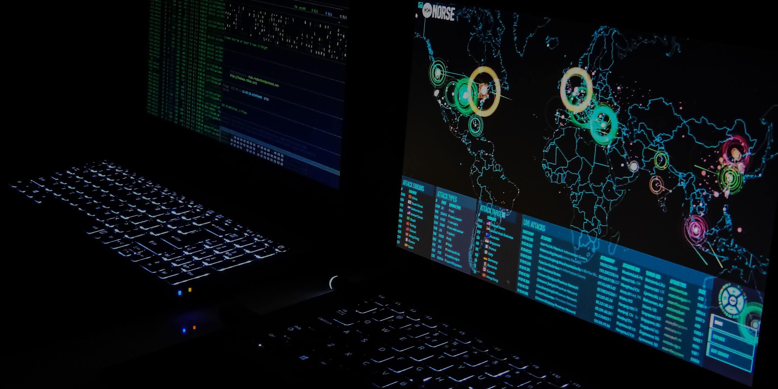 Two computer monitors, one displaying a map of the world, are visible in darkness.