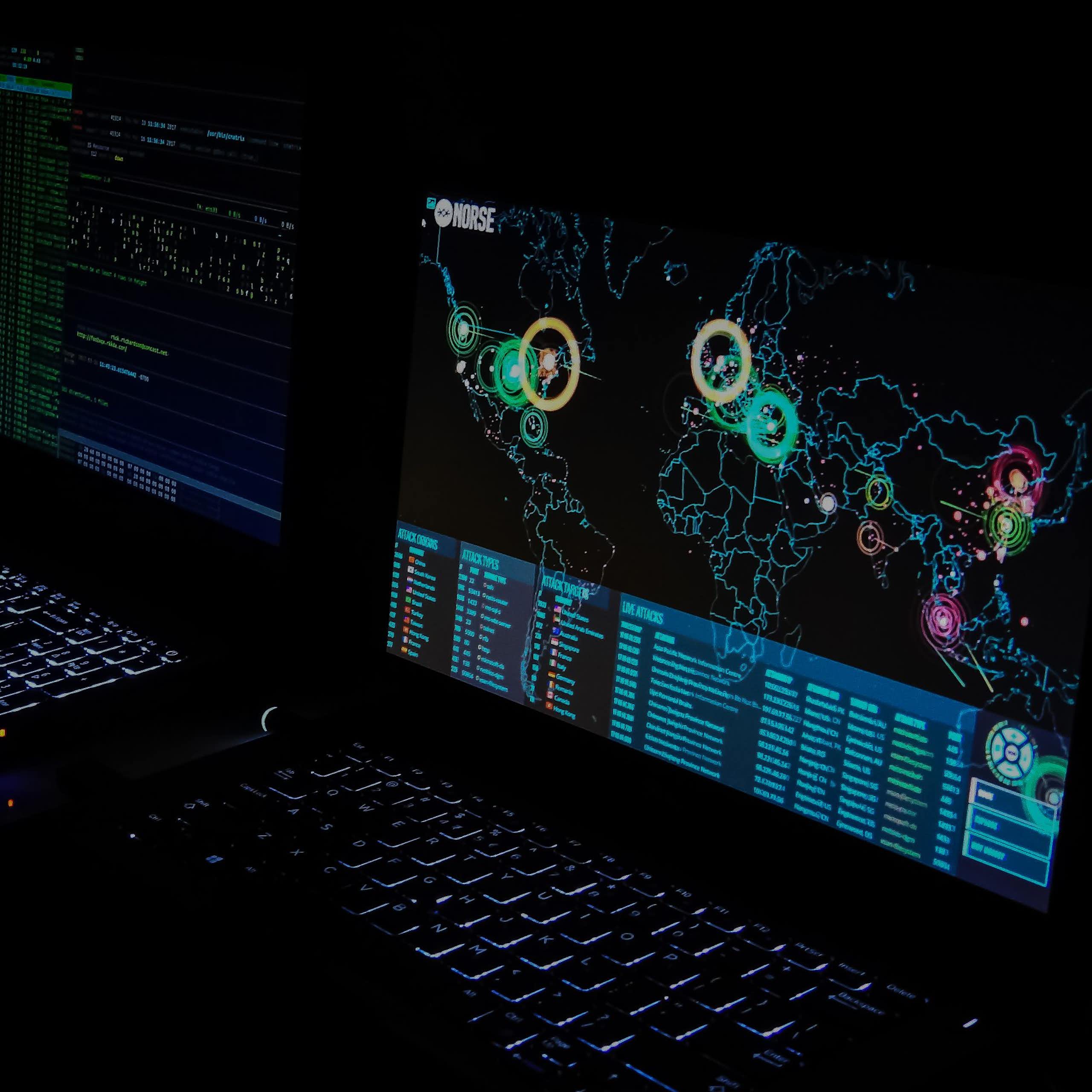Two computer monitors, one displaying a map of the world, are visible in darkness.