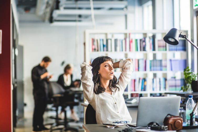 woman in an office leans back in her chair and looks into distance