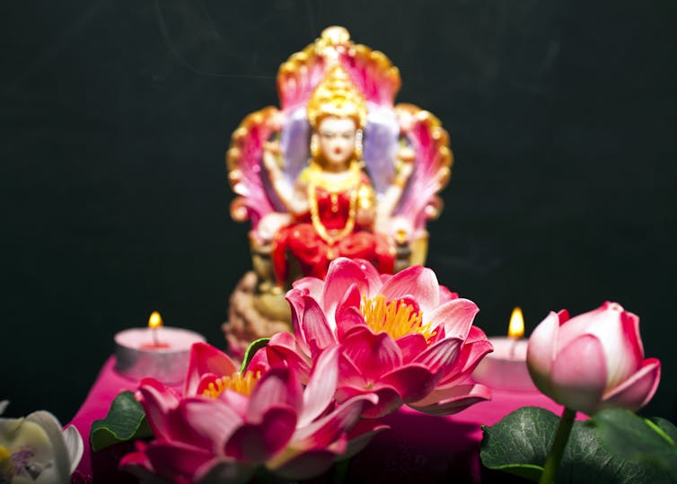 A Hindu goddess, dressed in a red saree, seated on a throne with lotus flowers in front.