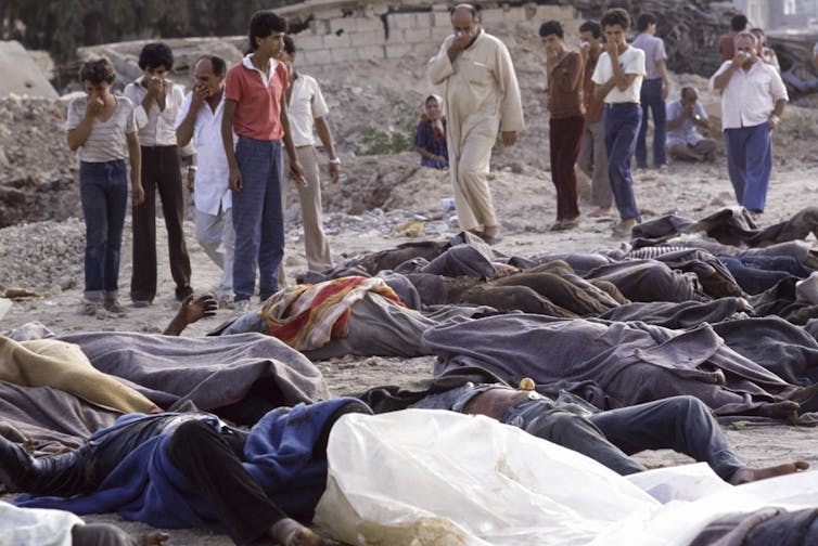 Bodies covered with blankets are seen as civilians look on.