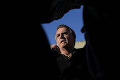 A man's face is framed by reporters in a media scrum.
