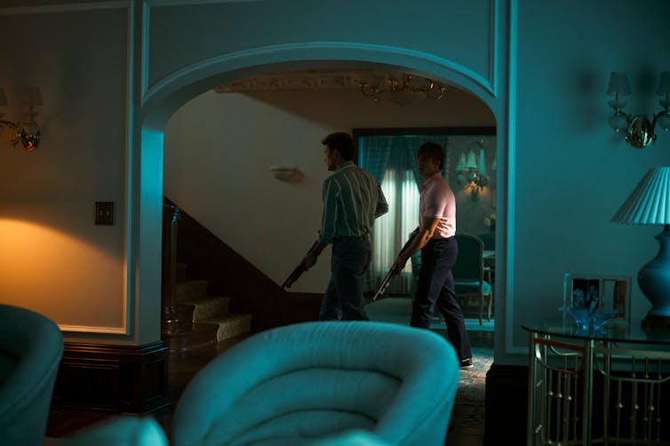A scene from a show depicts two young men walking in a dark house holding shotguns.