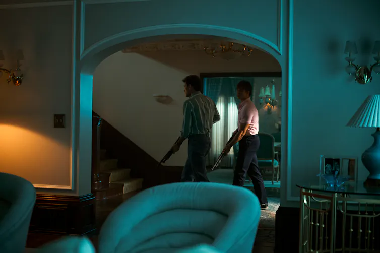 A scene from a show depicts two young men walking in a dark house holding shotguns.