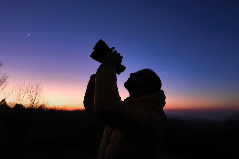A person looking up at the night sky with binoculars.
