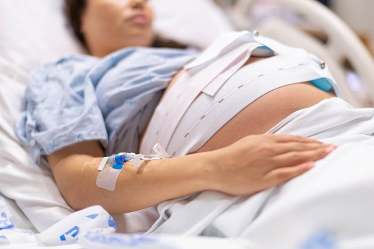 Pregnant woman lying in hospital bed, being monitored with band around her middle