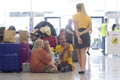Women and a man sitting on an airport floor