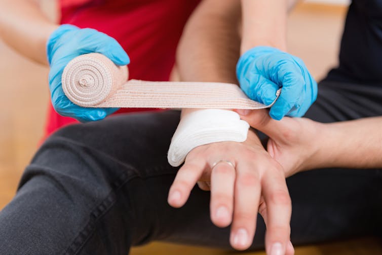person with gloves hands applies bandage of injured person's hand