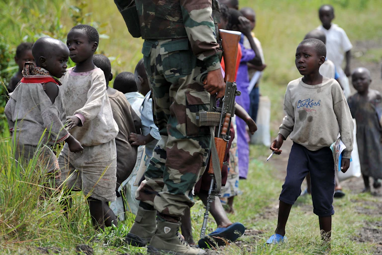 A group of children surrounding a man who is standing still while holding a gun
