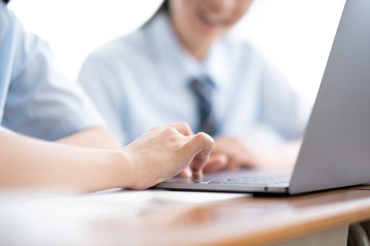 Two students in shirts and ties work on a laptop.