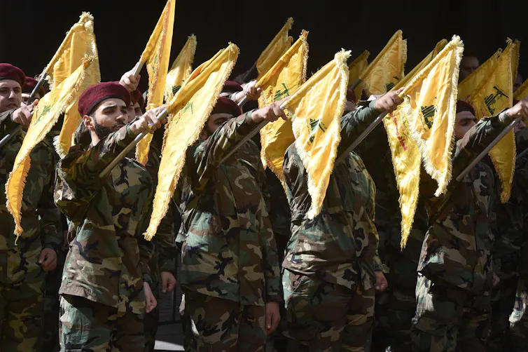 Hezbollah fighters stand at attention with flags at half mast to mourn dead comrades.