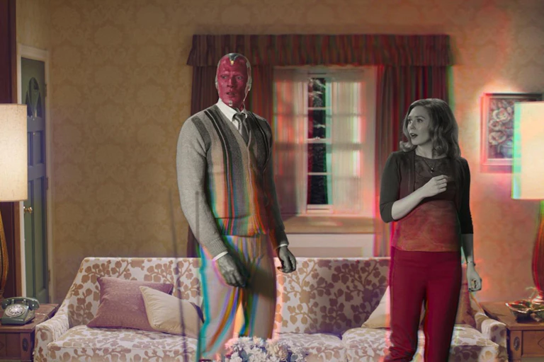 Una mujer y un robot, medio en blanco y negro medio en color, está de pie en un salón.