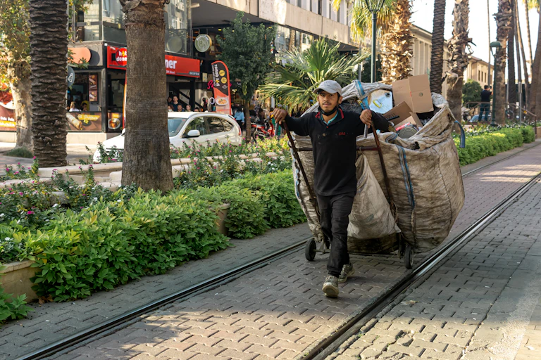 A waste picker walking down a street with a huge bag filled with rubbish.