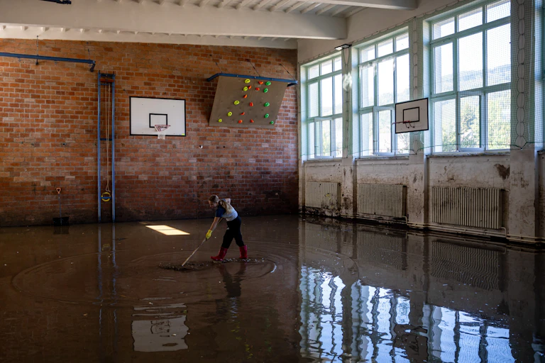 A person mopping up the floor in a flooded gymnasium.