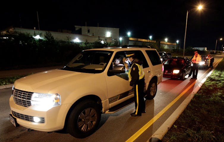 Uniformed police officers stop vehicles at night.