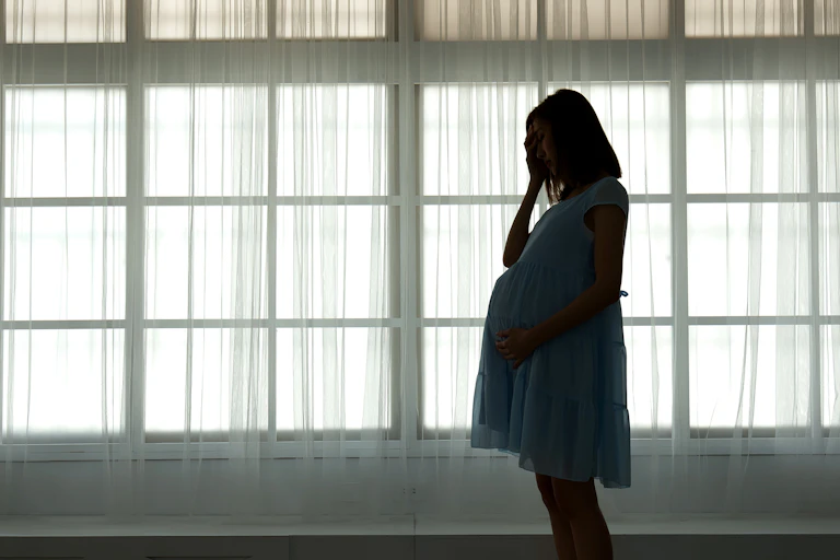 The silhouette of a pregnant woman holding a hand to her head