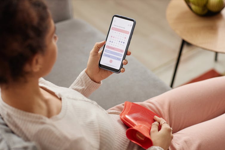 A woman looks at her period-tracking app while holding a hot water bottle.