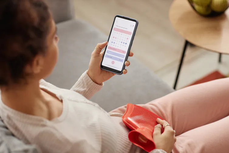 A woman looks at her period-tracking app while holding a hot water bottle.
