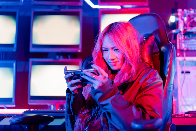 A young woman with pink hair sits in gaming chair frowning at her smartphone game.