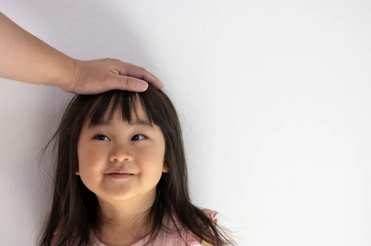 An adult pats a young girl on the head.