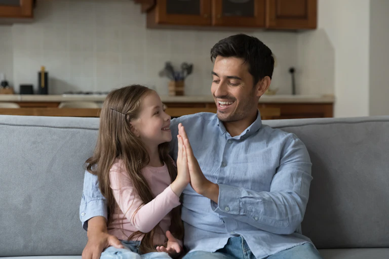 A man and girl do a high five while sitting on a couch.