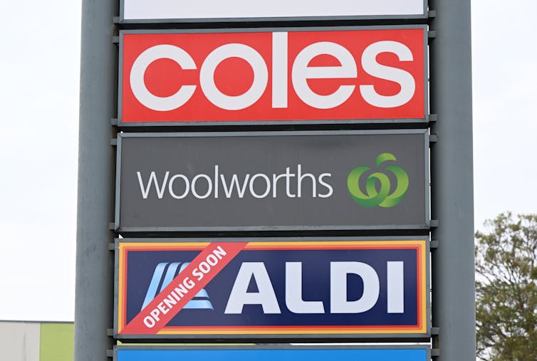A sign displays the logos of Coles, Woolworths and Aldi.