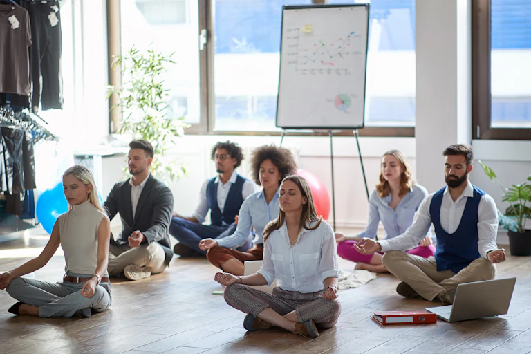 A group of employees in business attire sit on the floor and meditate in an office.
