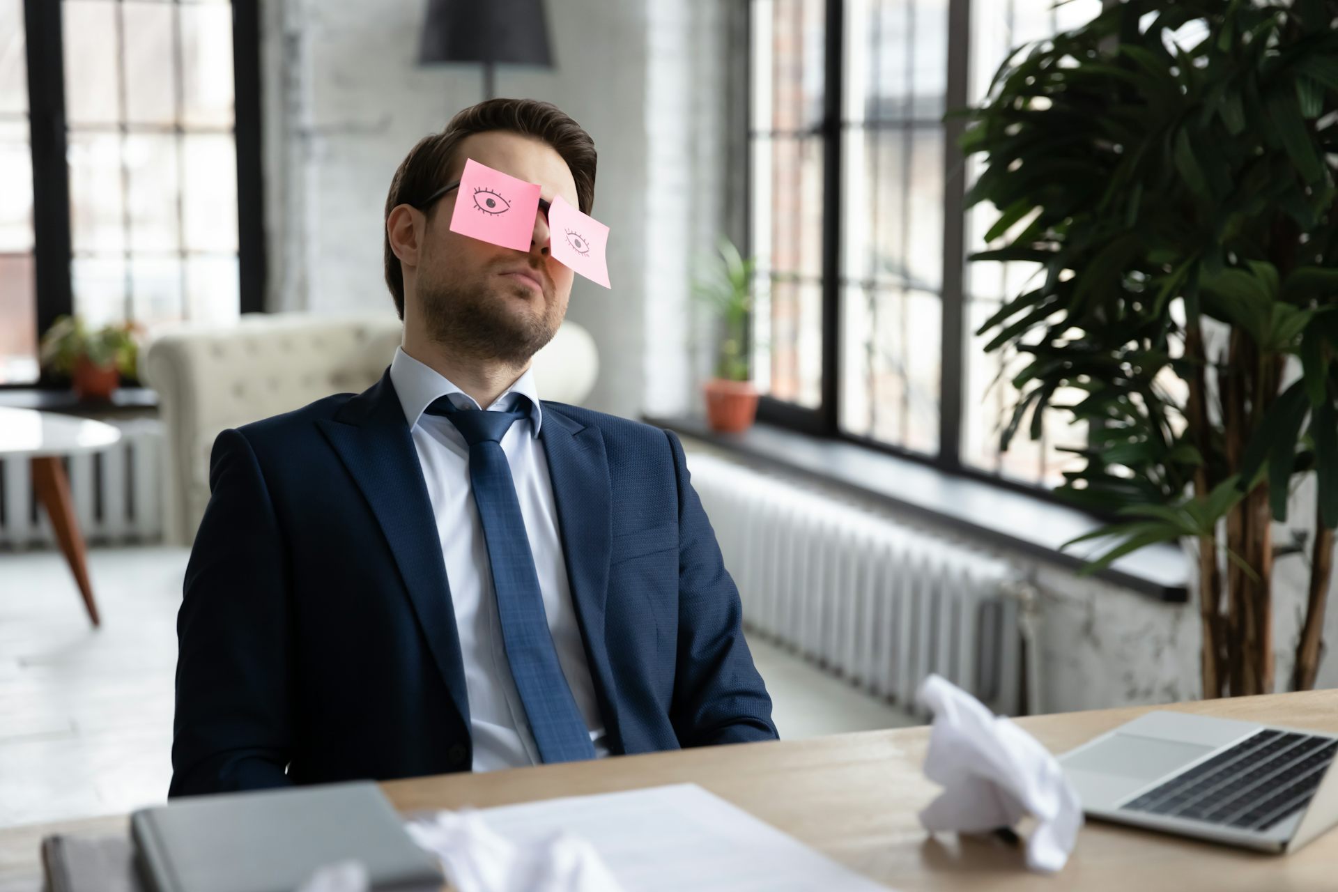 A bored employee leans back in his desk chair with post-it notes over his eyes.